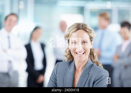 La clé du succès est une grande attitude. Riant femme d'affaires mûre avec son équipe d'affaires derrière elle - portrait. Banque D'Images