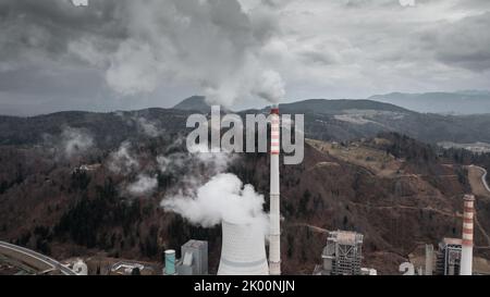 Cheminée et fumée épaisse provenant d'une tour de centrale thermique, une colline couverte de forêt en arrière-plan Banque D'Images