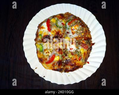 une pizza fraîche, chaude et colorée, placée dans une assiette blanche sur fond de bois Banque D'Images