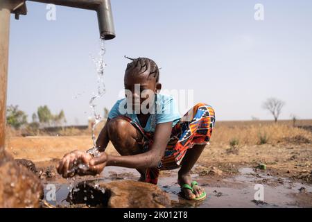 Une jeune fille africaine se croise à la légère devant une pompe à eau et se lave grossièrement, ce qui est symbolique du manque d'eau du robinet et d'installations de lavage Banque D'Images