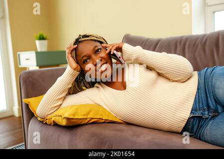 jeune femme afro-américaine utilisant un smartphone sur un canapé à la maison Banque D'Images