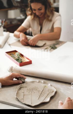 Femme décorant avec des fleurs roulé argile, faisant plaque en céramique en studio avec motif floral. Travail créatif fait main. Atelier de poterie pour adultes. Banque D'Images