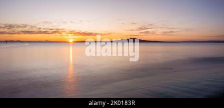 Soleil levant sur l'île Rangitoto à Milford Beach en hiver, Auckland. Banque D'Images