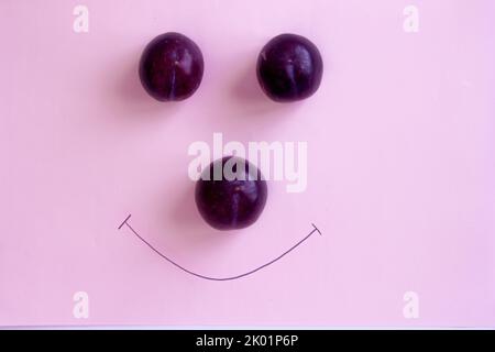 Damson prune sur fond rose isolé, sourire visage avec prunes rouges Banque D'Images