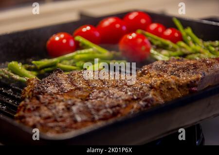 Steak de bœuf grillé sur une poêle à grillades noire, steak de bœuf avec tomates et asperges, vue rapprochée et mise au point sélective Banque D'Images
