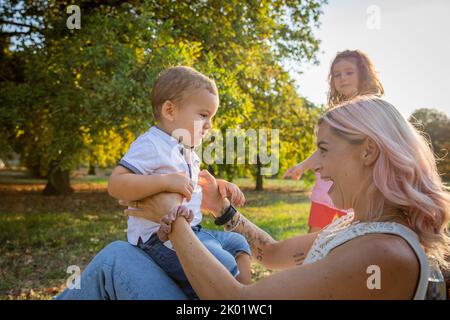 Mère joue avec son fils et le fait s'asseoir sur ses genoux, la fille à l'arrière-plan, la relation de mère avec ses enfants Banque D'Images