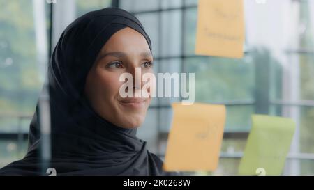 Jeune femme responsable de bureau regarder la planification verre conseil confiant satisfait femme d'affaires cadre examine des notes sur collantes de couleur Banque D'Images