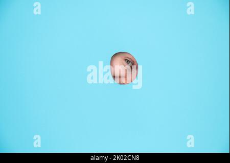 Une femme piquant hors de trou dans fond de papier bleu. Banque D'Images