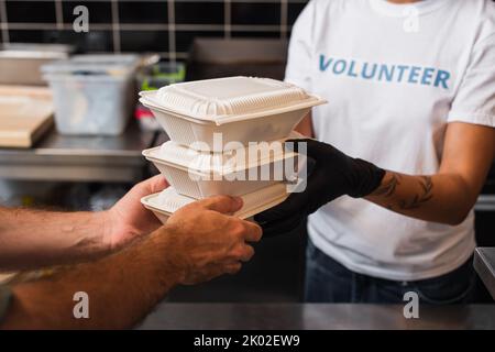 vue rognée du volontaire afro-américain donnant des récipients en plastique avec de la nourriture à l'homme, image de stock Banque D'Images