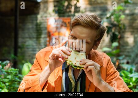 homme gai et roux mangeant de savoureux quesadilla dans une tortilla croustillante, image de stock Banque D'Images