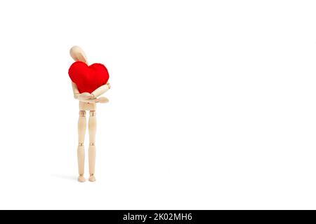 Un mannequin en bois enchâssant un coeur en tissu rouge sur un fond blanc Banque D'Images