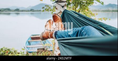Jeune femme cuir mode bottes photo. Femelle balançant dans un hamac entre les bouleaux sur la rive du lac de montagne. Loisirs en plein air à l'extérieur de la ville Banque D'Images