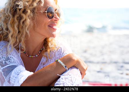 Gros plan portrait de femme souriant et profitant du soleil à la plage pendant les vacances d'été. Tourisme de femmes avec des lunettes de soleil et des cheveux blonds de style surfeur. Bonne et heureuse jeune femme Banque D'Images