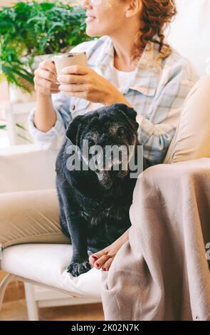 Portrait du chien noir et de la femme propriétaire en train de se détendre à la maison assis sur la même chaise. Concept de meilleur compagnon de freind et de vie. Couple personnes animal dans l'amitié Banque D'Images