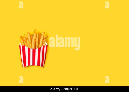 Pommes de terre frites dans une boîte rayée rouge et blanche sur fond jaune avec espace de copie Banque D'Images