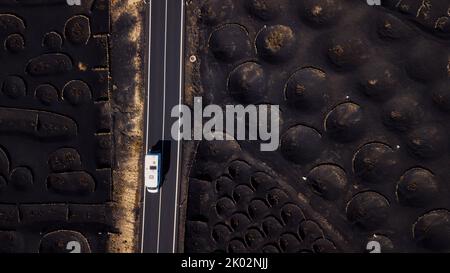 Minibus blanc de camping voyageant et conduisant sur une longue route droite dans un endroit volcanique pittoresque. Au-dessus de drone vue aérienne de personnes et de Voyage concept. Sol volcanique de sable noir vu de la vue verticale Banque D'Images