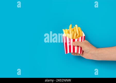 Homme tenant une boîte rayée avec des pommes de terre frites sur fond bleu avec copie de sapce Banque D'Images