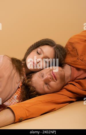 vue de dessus de jeune homme heureux avec les yeux fermés couché avec une jolie petite amie sur beige, image de stock Banque D'Images