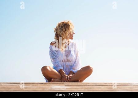 Jolie femme élégante avec robe de boho de plage blanche assise sur la jetée en bois outdor, Portrait de touriste appréciant l'extérieur et vacances d'été. Détendez-vous dans l'espace de copie Banque D'Images