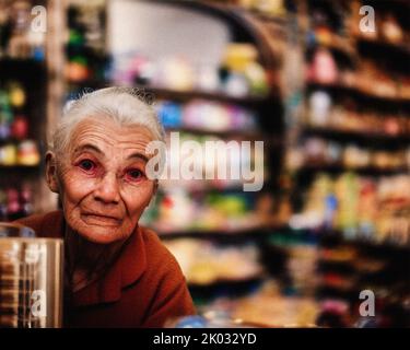 Une femme âgée derrière le comptoir dans un dépanneur Banque D'Images