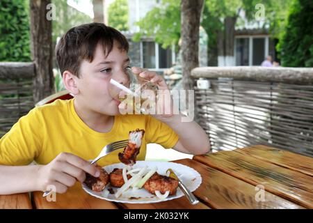 Garçon mangeant du kebab au cou de porc sur la terrasse du restaurant Banque D'Images