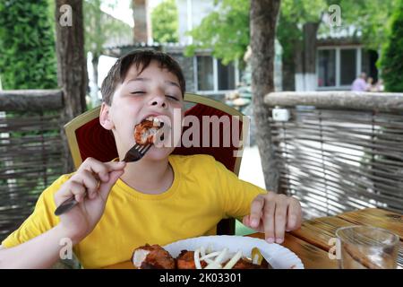 Enfant mangeant du kebab au cou de porc sur la terrasse du restaurant Banque D'Images