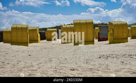 Un ensemble de chaises de plage à capuchon sur le sable sous la lumière du soleil avec ciel nuageux Banque D'Images