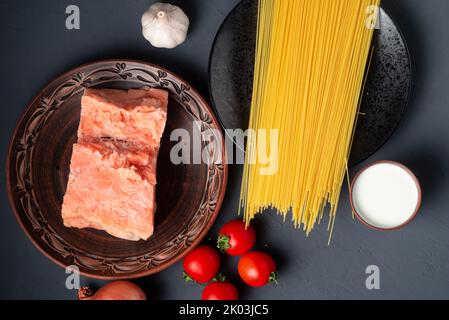 Ingrédients pour la préparation de spaghetti au saumon et aux tomates. Un ensemble de produits - saumon congelé, ail, crème sur fond gris. Banque D'Images