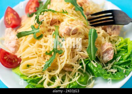 Spaghetti au saumon, fromage sur une salade de laitue arrosée d'arugula et de tomates cerises en gros plan Banque D'Images