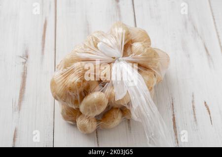 Jeunes pommes de terre dans un sac transparent en plastique sur fond clair en bois. Banque D'Images