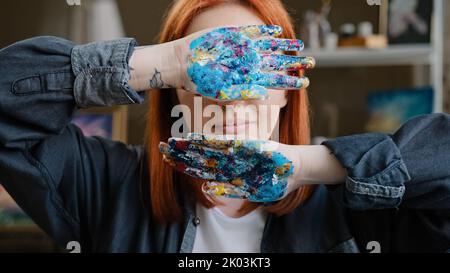 Gros plan enfant étudiant classe d'art dame caucasien rouge-cheveux fille artiste femme peintre designer montrant des palmiers sales dans les peintures tenant les mains couvertures Banque D'Images