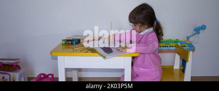 Adorable petite fille avec un tablier rose colorant un cahier. Retour à l'école primaire et à la maternelle. Bannière horizontale Banque D'Images