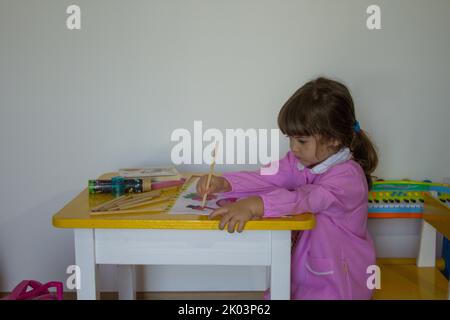 Adorable petite fille avec un tablier rose colorant un cahier. Retour à l'école primaire et à la maternelle Banque D'Images