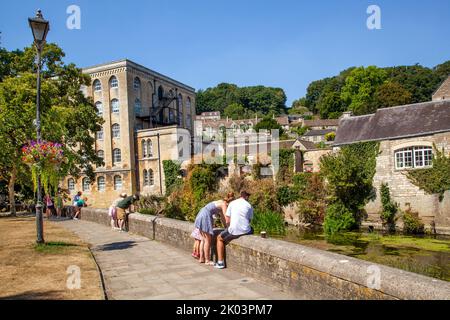 Les gens sur la promenade le long des rives de la rivière Avon à Bradford sur Avon Wiltshire avec une vue sur l'ancien moulin de l'abbaye Banque D'Images