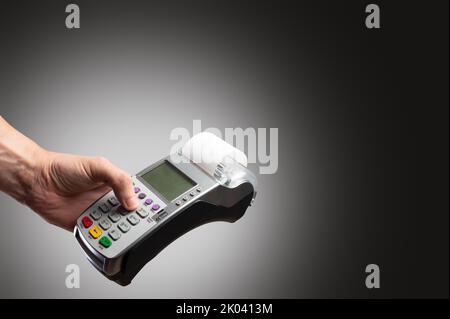 Cash terminal dans la main d'un homme sur un fond gris. Minimalisme. Opérations commerciales, ventes en gros et au détail, achats, ventes et achats en ligne, Banque D'Images