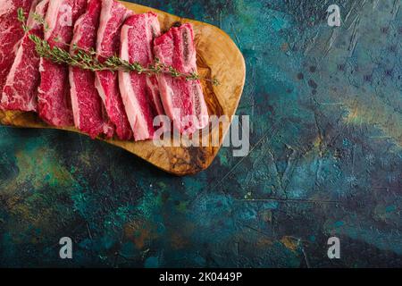 Sur fond de marbre, les steaks de viande sur une planche à découper en bois sont prêts à cuire. Restaurant, hôtel, café, cuisine maison. Il y a de l'espace libre pour INS Banque D'Images