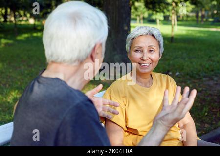 Couple d'âge moyen les conjoints multiethniques s'assoient sur le banc profiter de parler dans le parc public d'été avoir une conversation amicale partager des pensées ou des nouvelles pendant Banque D'Images