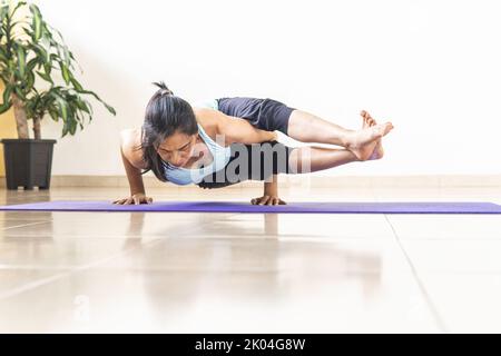Femme mature pratiquant le yoga, Astavakrasana ou posture à huit angles sur un tapis Banque D'Images