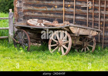 Un vieux wagon en bois se dresse sur de l'herbe verte d'été près d'un mur en bois rural Banque D'Images