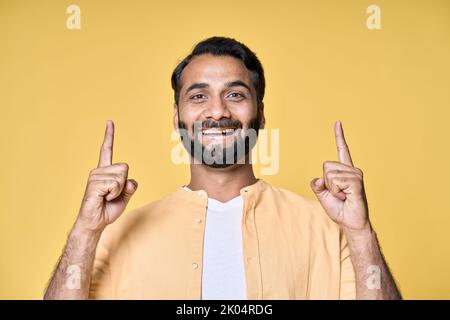 Homme indien souriant pointant du doigt vers le haut de la publicité isolée sur fond jaune. Banque D'Images