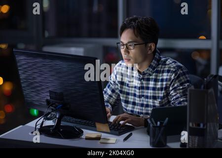Travailleur informatique chinois travaillant au bureau la nuit Banque D'Images