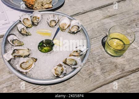 Assiette avec huîtres fraîches ouvertes sur la glace, table en bois dans un café rustique extérieur, lumière naturelle Banque D'Images