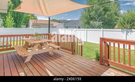 Panorama Whispy White Clouds terrasse en bois avec un parasol sur la table avec des banquettes. Terrasse à l'arrière-cour d'une maison avec vue sur une pelouse et wh Banque D'Images