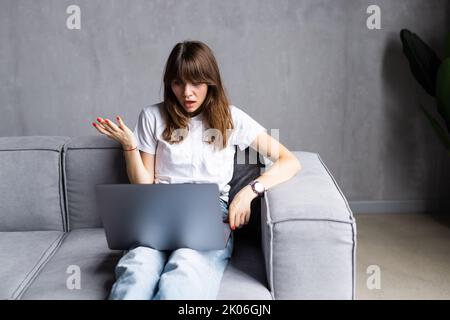 Une femme excitée qui se montre à l'écran, criant pour la joie, le souffle, riant, tenant la tête dans l'étonnement, surprise, obtenant de bonnes nouvelles impressionnantes, assis Banque D'Images