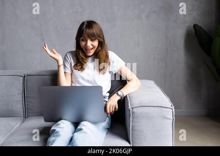 Une femme excitée qui se montre à l'écran, criant pour la joie, le souffle, riant, tenant la tête dans l'étonnement, surprise, obtenant de bonnes nouvelles impressionnantes, assis Banque D'Images