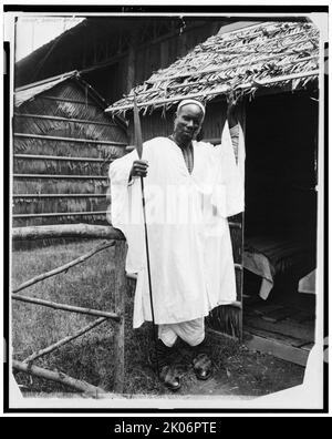 Chef, Afrique la plus sombre, 1901. Chef africain, à part entière, debout à l'extérieur de la hutte de chaume, tenant la lance, à l'exposition panaméricaine, Buffalo, N.Y. Banque D'Images