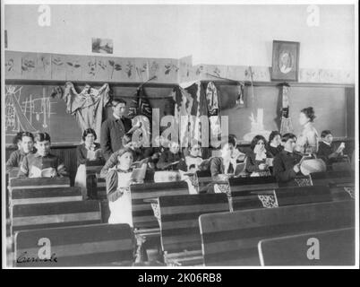 Élèves de sexe masculin et féminin lisant en classe, Carlisle Indian School, Carlisle, Pennsylvanie, 1901. (Pensionnat pour étudiants amérindiens, fondé en 1879 sous l'autorité gouvernementale des États-Unis. Notez les vêtements traditionnels attachés au mur, et le dessin de tipi sur le tableau noir). Banque D'Images