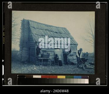 Ancienne cabine, 1899 ou 1900. La photo montre deux hommes afro-américains et une femme afro-américaine à l'extérieur d'une cabine, un homme hache du bois. Dans la variante, sur l'épaule gauche de l'homme hacher du bois se trouve un homme assis sur un chariot tiré par des chevaux. Banque D'Images