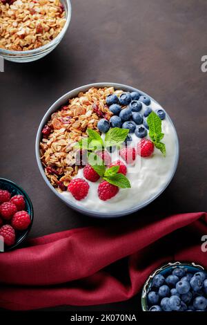 Yaourt avec granola et baies dans un bol. Composition avec petit déjeuner sain et ingrédients avec serviette bordeaux. Pose à plat Banque D'Images