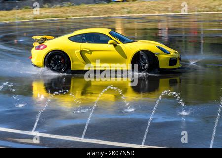 Voiture de sport voiture de course Porsche Cayman GT4 sur piste de pluie dérivant à travers l'asphalte humide pendant l'entraînement à la sécurité de conduite, dans l'eau de premier plan Banque D'Images
